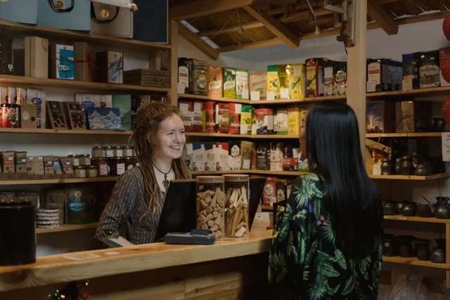 Friendly shopkeeper assisting a customer in a cozy, well-stocked store environment. Network marketing training: retail-first practice