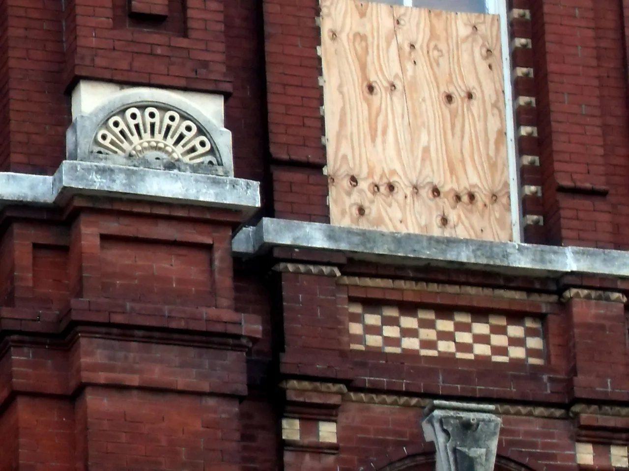 Upper facade of a boarded brick storefront.