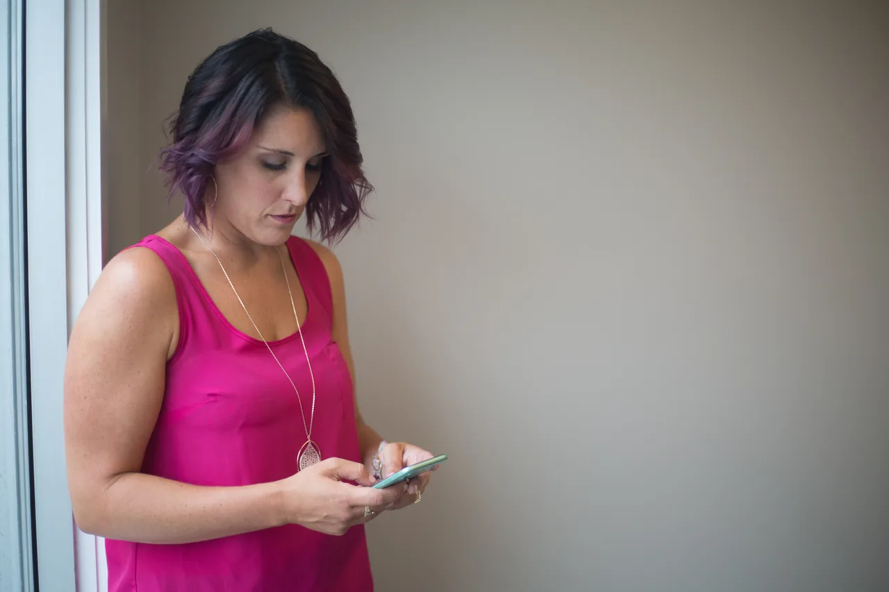 A woman writes a message on a smartphone outdoors.